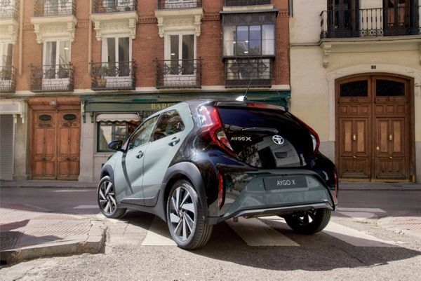 Image showin gthe tarragon Green Aygo X driving away around a corner in the city